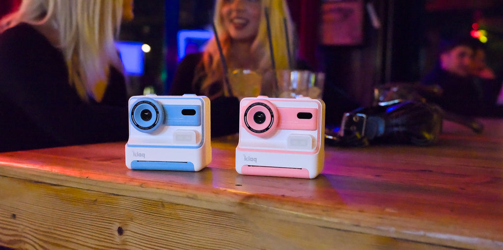 Two instant cameras on a wooden surface with a blurred background