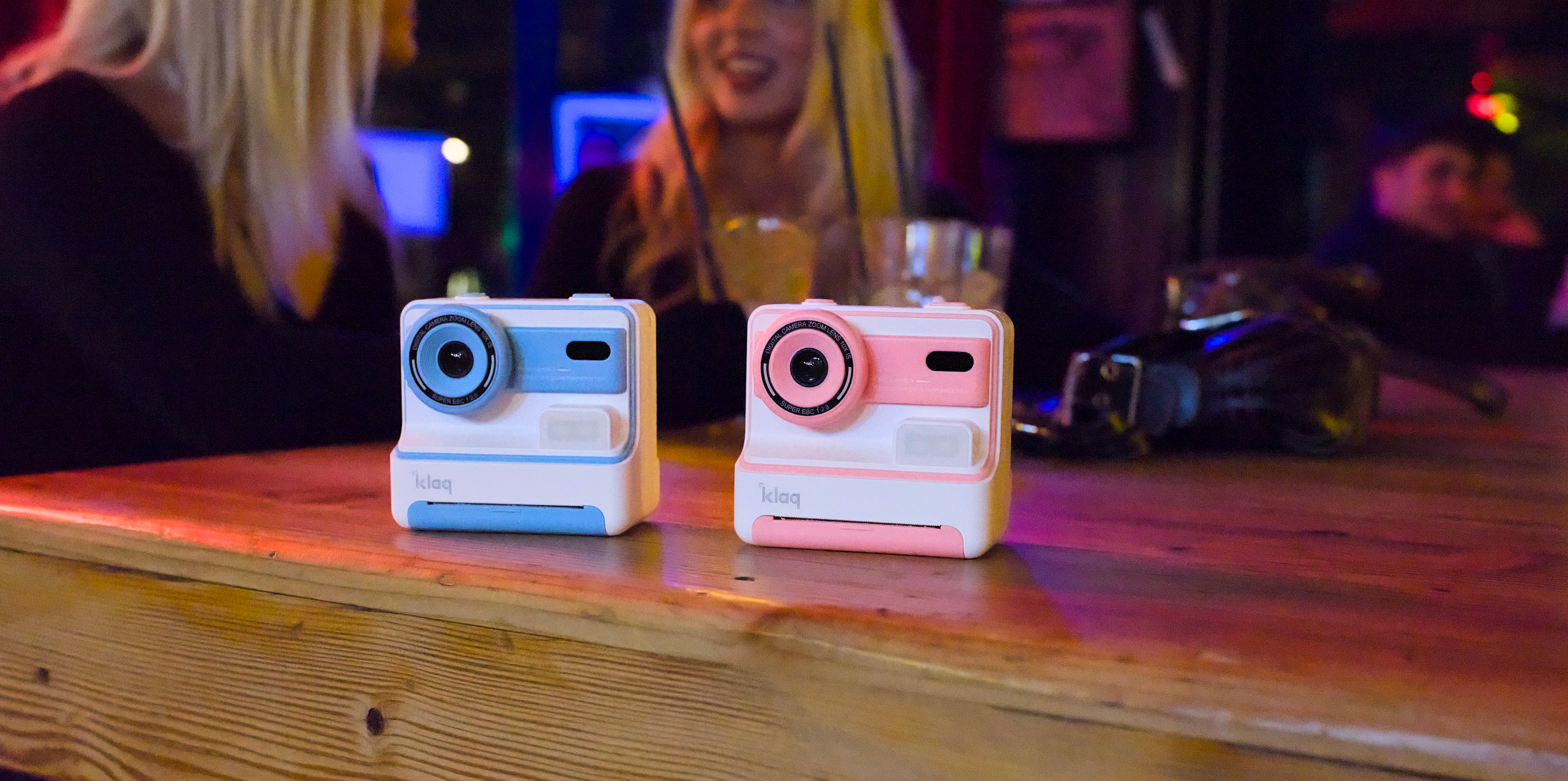 Two instant cameras on a wooden surface with a blurred background